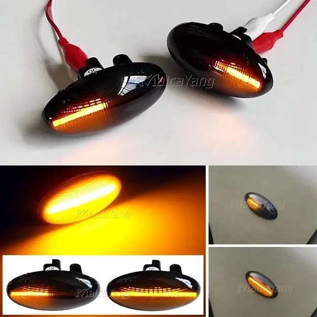 Pair of amber motorcycle turn signal lights with black oval housings and red wiring lit with orange glow on a white surface